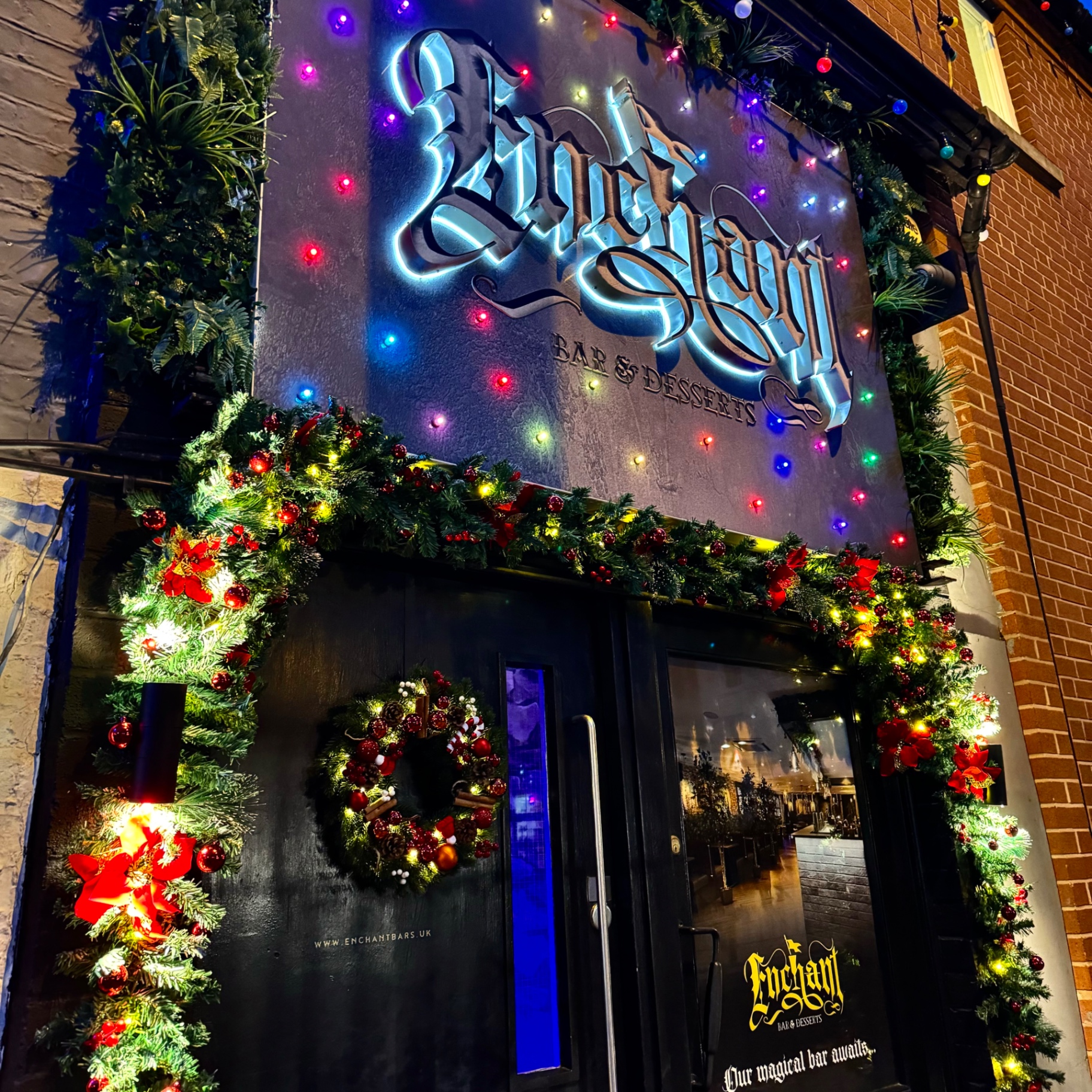 The Enchant sign glowing above the Christmas-decorated entrance